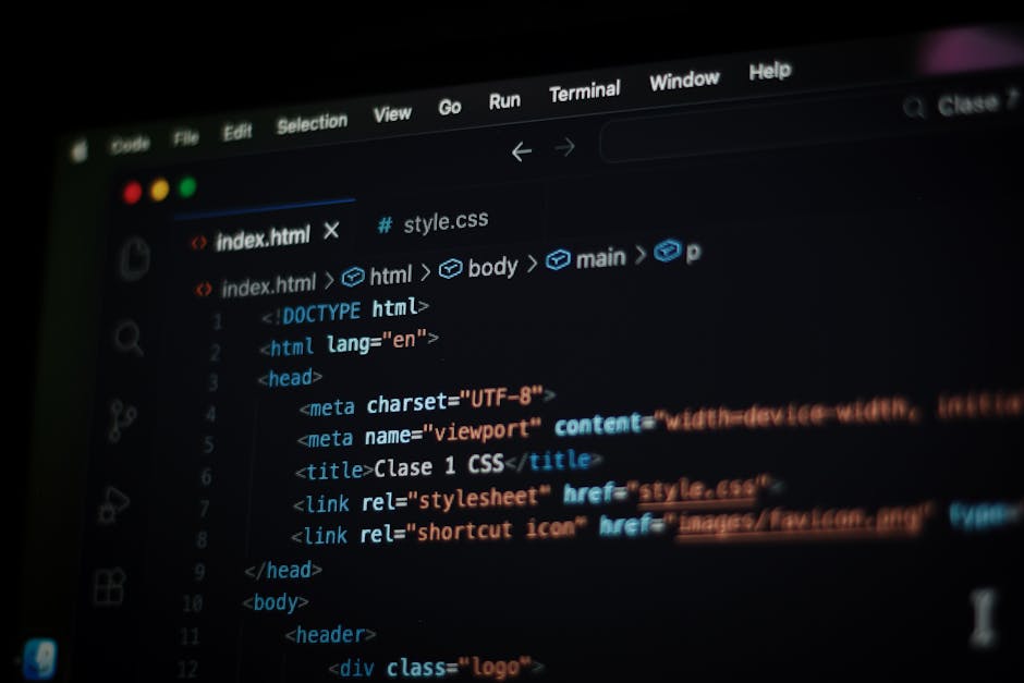 A computer workstation in a workspace or office environment featuring a central flat-screen monitor displaying lines of code in various colors on a dark background. The monitor is surrounded by a wire