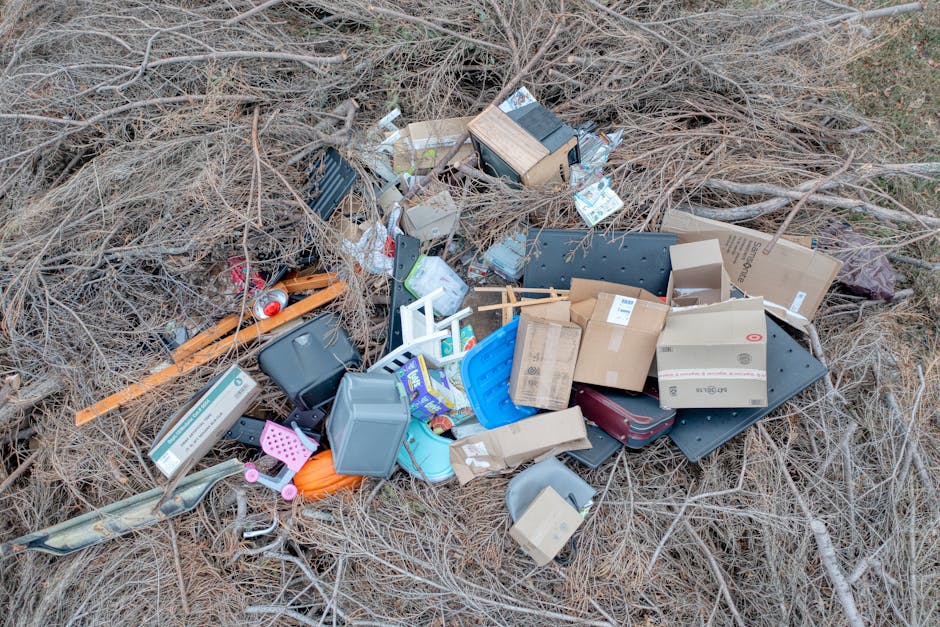 A collection of overflowing rubbish bins and scattered waste surrounding a large grey mixed paper and card recycling container situated on a paved urban street. The recycling bin is partially open, re