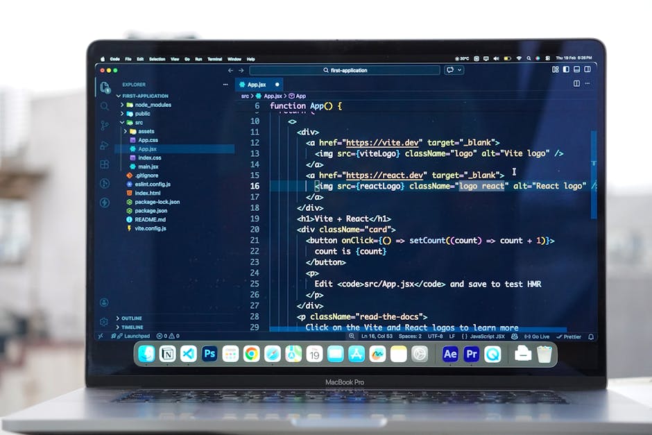 A close-up view of a MacBook Pro laptop on a white surface showing a coding environment on its screen, with a dark theme background and syntax-highlighted JavaScript code. The code includes HTML marku